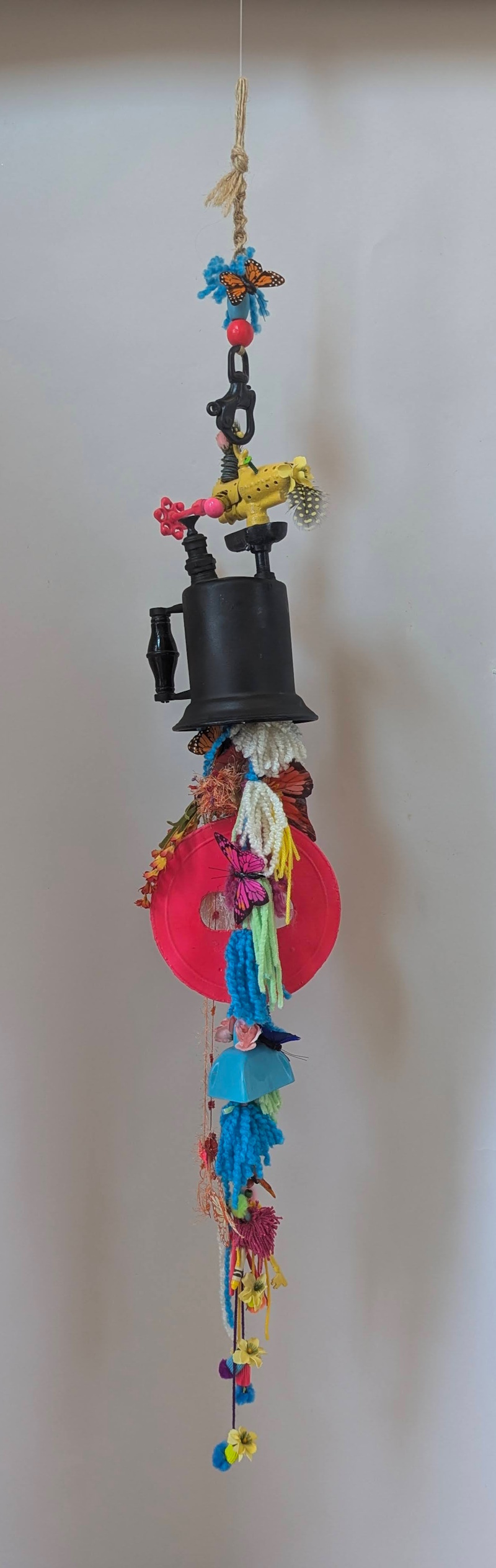 Childhood assemblage sculpture made from an antique oilcan decorated with colorful feathers, butterflies, flowers, and large pink beads.
